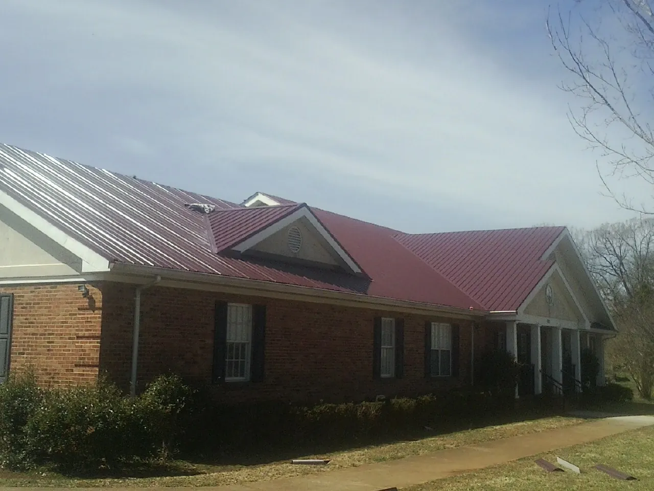 Red metal roof with gabled entries on a long brick building, from a Hail Damage Roof Repair job in Littlerock