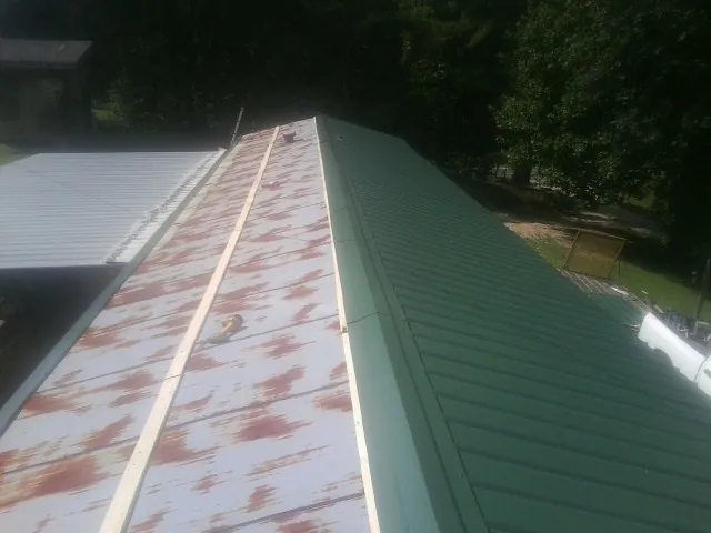 Old rusted panels beside newly installed green metal roofing — Wind Damage Roof Repair by Roofing Brothers in Littlerock