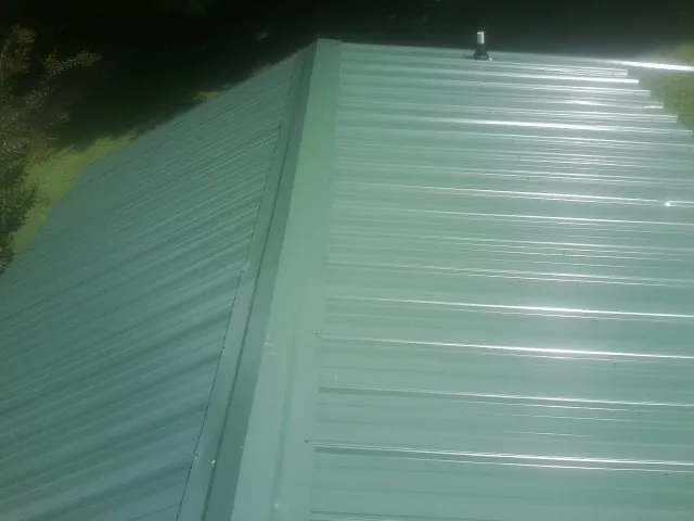New green metal panels meeting at the ridge of a roof — Flat Roof Repair work by our crew in Littlerock