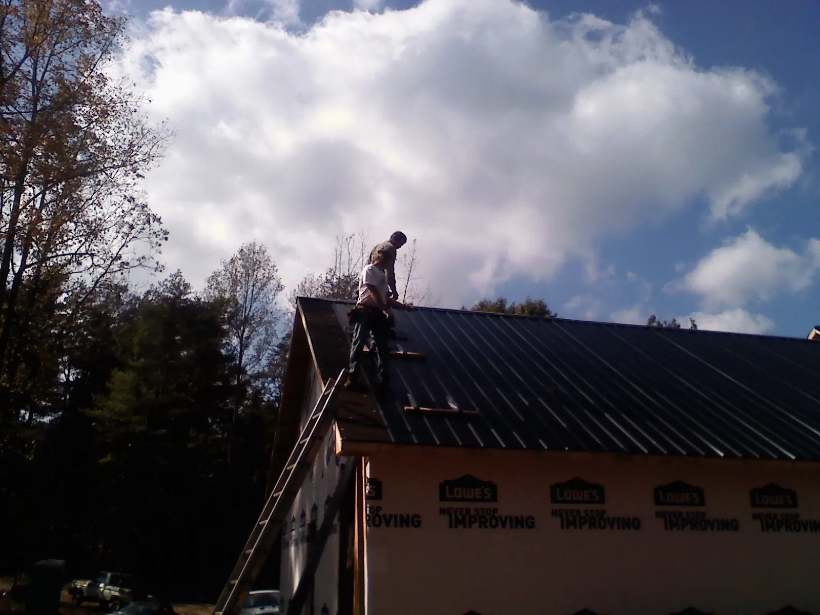Roofer fastening dark metal panels high against a cloudy sky, from a Roof Inspection job in Littlerock